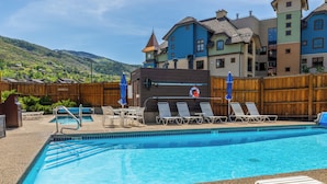 Une piscine entourée d’une clôture en bois, avec des chaises longues et des parasols.
