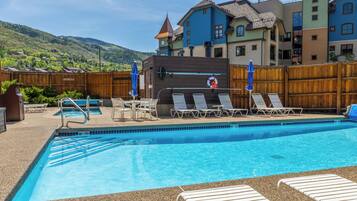 A swimming pool with lounge chairs and umbrellas, surrounded by a wooden fence.