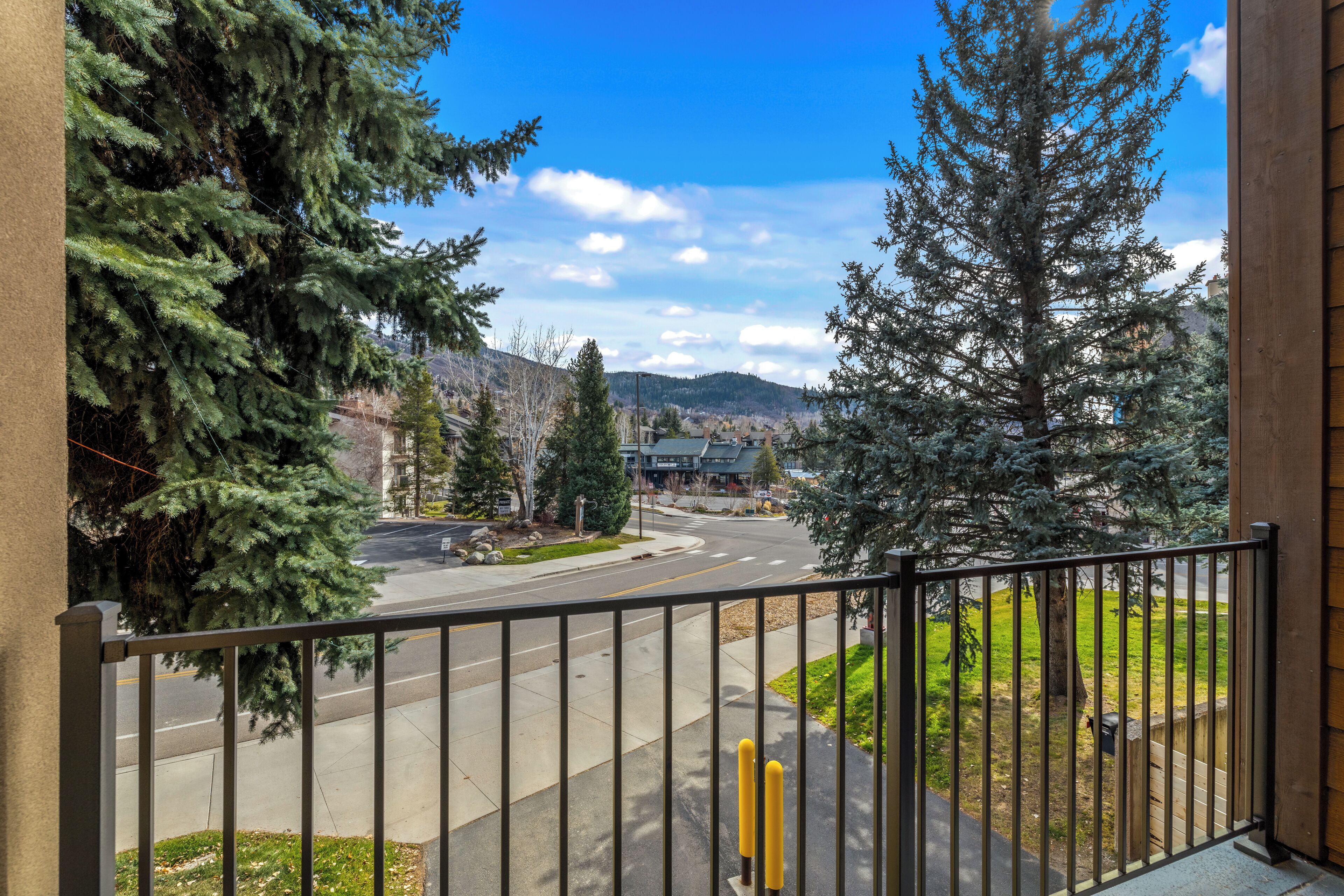 A balcony with a view of a street, trees, and a distant mountain range.