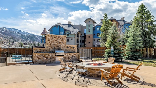 A patio with outdoor furniture and a fire pit, surrounded by a stone wall and a wooden fence. - Base Area Condo | Steps to Ski | Pool and Hot Tub (Steamboat Springs)