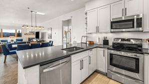 A modern kitchen with stainless steel appliances, white cabinetry, and a black countertop. - Base Area Condo | Steps to Ski | Pool and Hot Tub (Steamboat Springs)