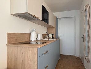 Een kleine keuken met een houten aanrecht, een inbouwfornuis en een magnetron. Er is een deur naar een andere kamer.