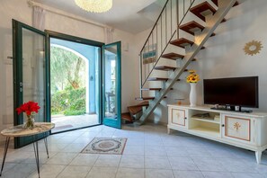 A living room with a TV, a staircase, a glass door leading outside, and a small table with flowers. - Holiday Home "La Casa 3m L" with Shared Pool, Wi-Fi and Air Conditioning (Santa Maria Coghinas)