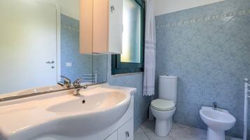 A bathroom with a sink, toilet, bidet, and a window with a curtain.