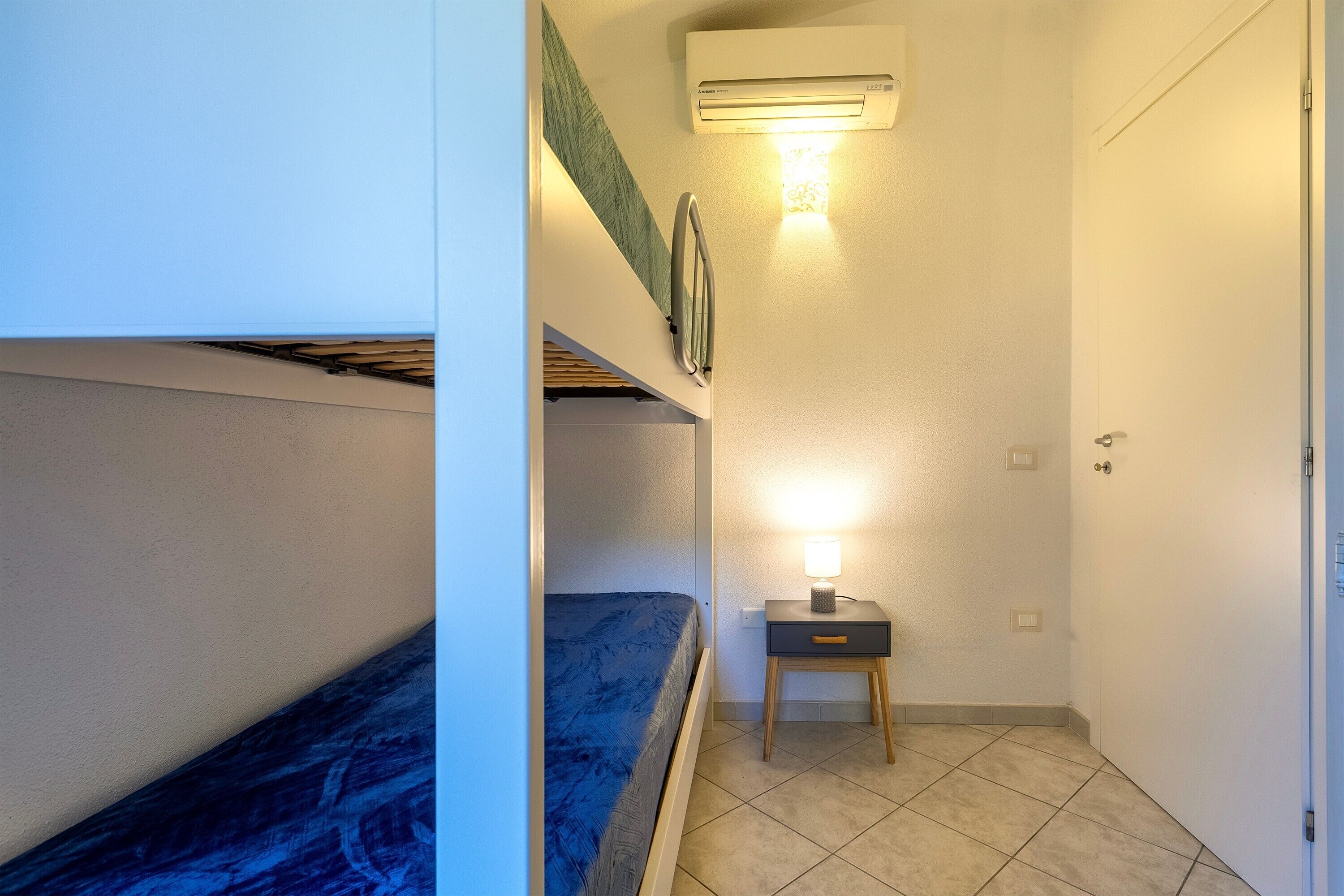 Ein kleines, gemütliches Schlafzimmer mit Etagenbetten, einem Nachttisch mit Lampe und einer Wandaircondition.