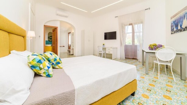 A hotel room with a bed, a desk, a chair, and a TV on the wall. - Sara Luxury Rooms - Positano Room (Meta)