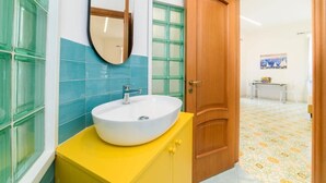 A bathroom with a white sink, a mirror, and a wooden door. - Sara Luxury Rooms - Positano Room (Meta)