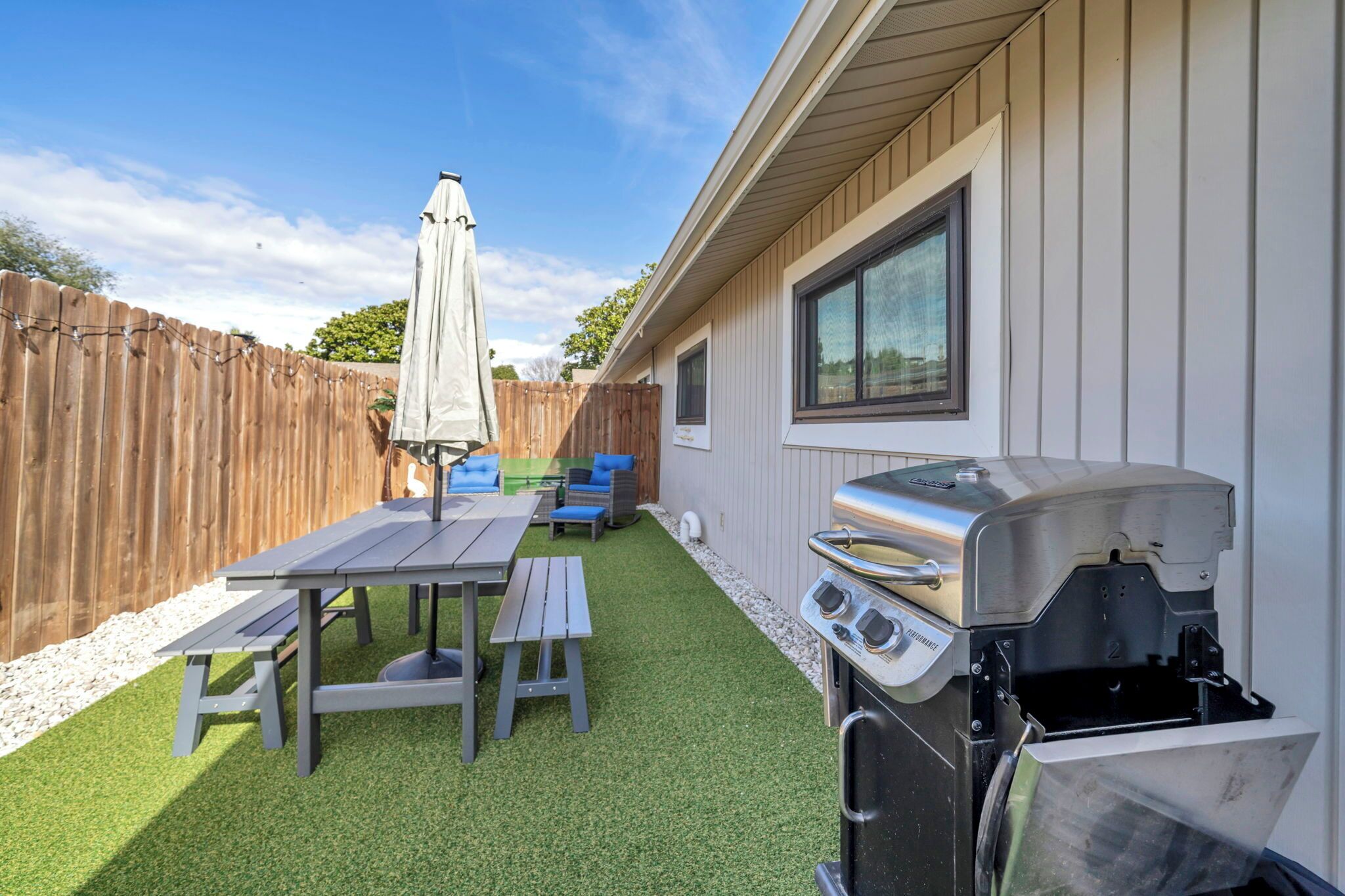 A backyard with a barbecue grill, a picnic table with benches, and a wooden fence.