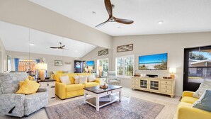 A spacious living room with a yellow sofa, a patterned armchair, and a coffee table. - Wavy Seas - Tennis Villa 77A (Miramar Beach)