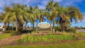 A sign for 'Searscape Tennis Village' surrounded by palm trees and a landscaped garden. - Wavy Seas - Tennis Villa 77A (Miramar Beach)