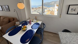 Ein Essbereich mit Tisch, Stühlen und Blick auf eine Küstenstadt durch ein Fenster.