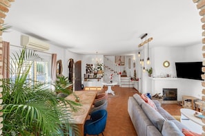 A spacious living area with a fireplace, a dining table with chairs, a sofa, and a TV mounted on the wall.