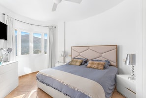A bedroom with a bed, bedside tables, a TV, and a window with curtains.
