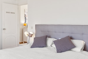 Ein Schlafzimmer mit einem Bett, zwei Kissen, einem Nachttisch, einer Lampe und einer Tür.