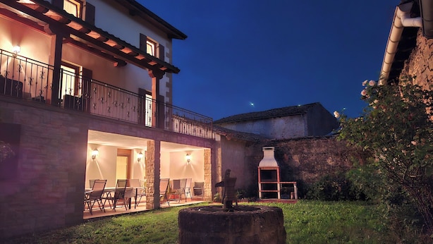 A two-story building with a balcony, outdoor seating area, and a stone chimney. - This is a peaceful place to stay: relax with the whole family! (Urroz-Villa)