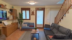 A living room with a blue sofa, a grey sofa, a wooden cabinet, a television, and a staircase. - This is a peaceful place to stay: relax with the whole family! (Urroz-Villa)