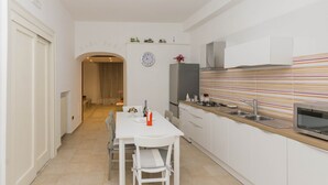 Een moderne keuken met witte kasten, een gestreept aanrecht en een eethoek met een witte tafel en stoelen.