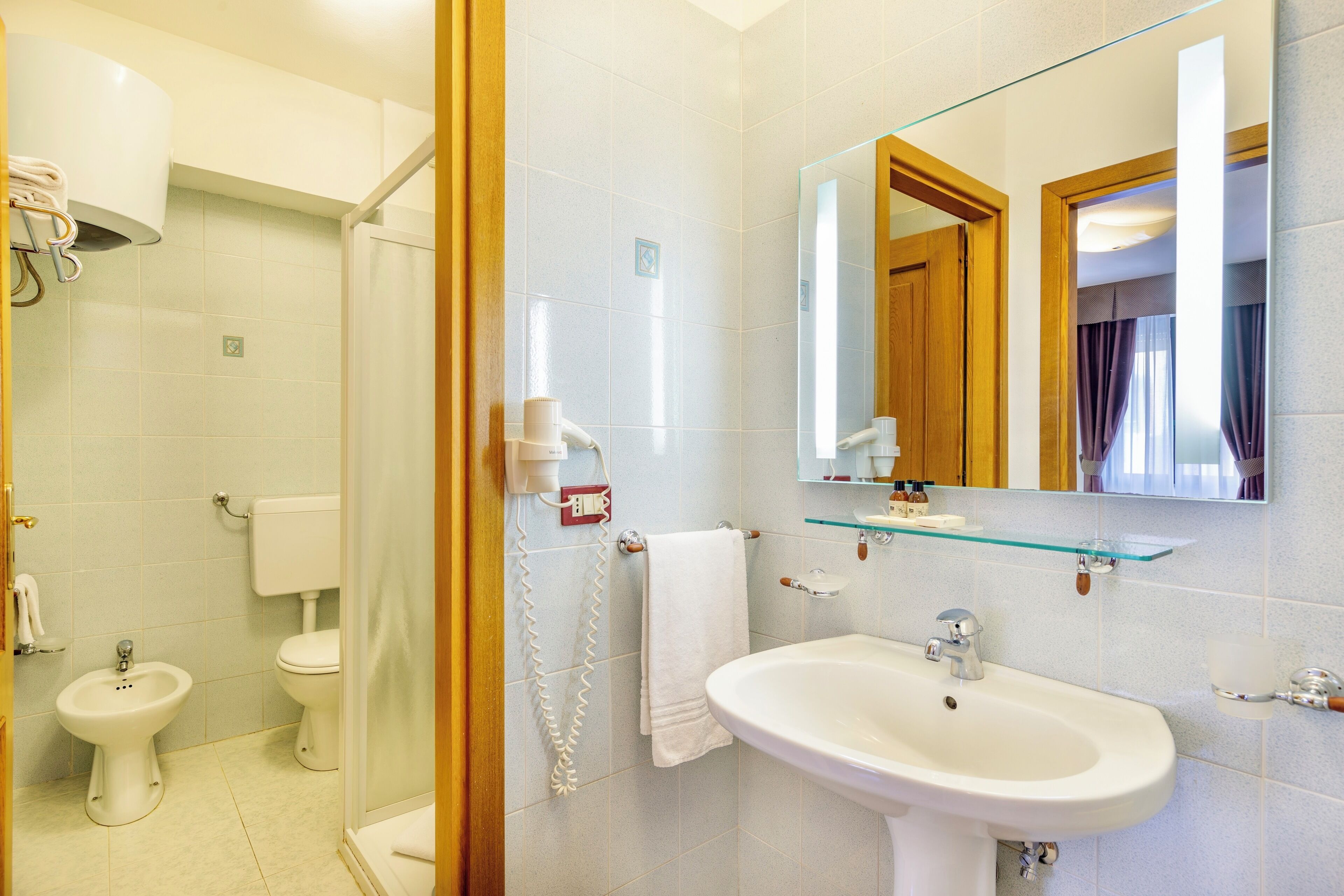 Un bagno con cabina doccia in vetro, un WC, un bidet, un lavandino e uno specchio.