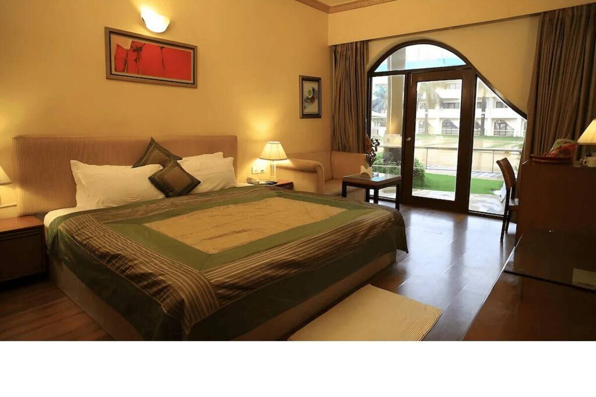 Camera d'albergo con un letto grande, un comodino, una scrivania e vista su un cortile attraverso una porta vetrata.