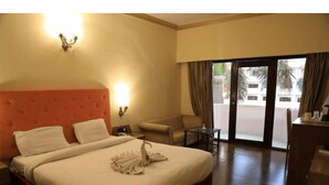 A hotel room with a large bed, a desk, a chair, and a view of the outside. - Swiss Traffalgaar Luxury Hotels (Nashik)