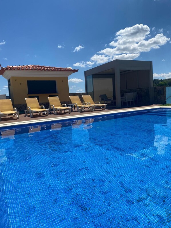 A swimming pool with lounge chairs and a modern building with a tiled roof.