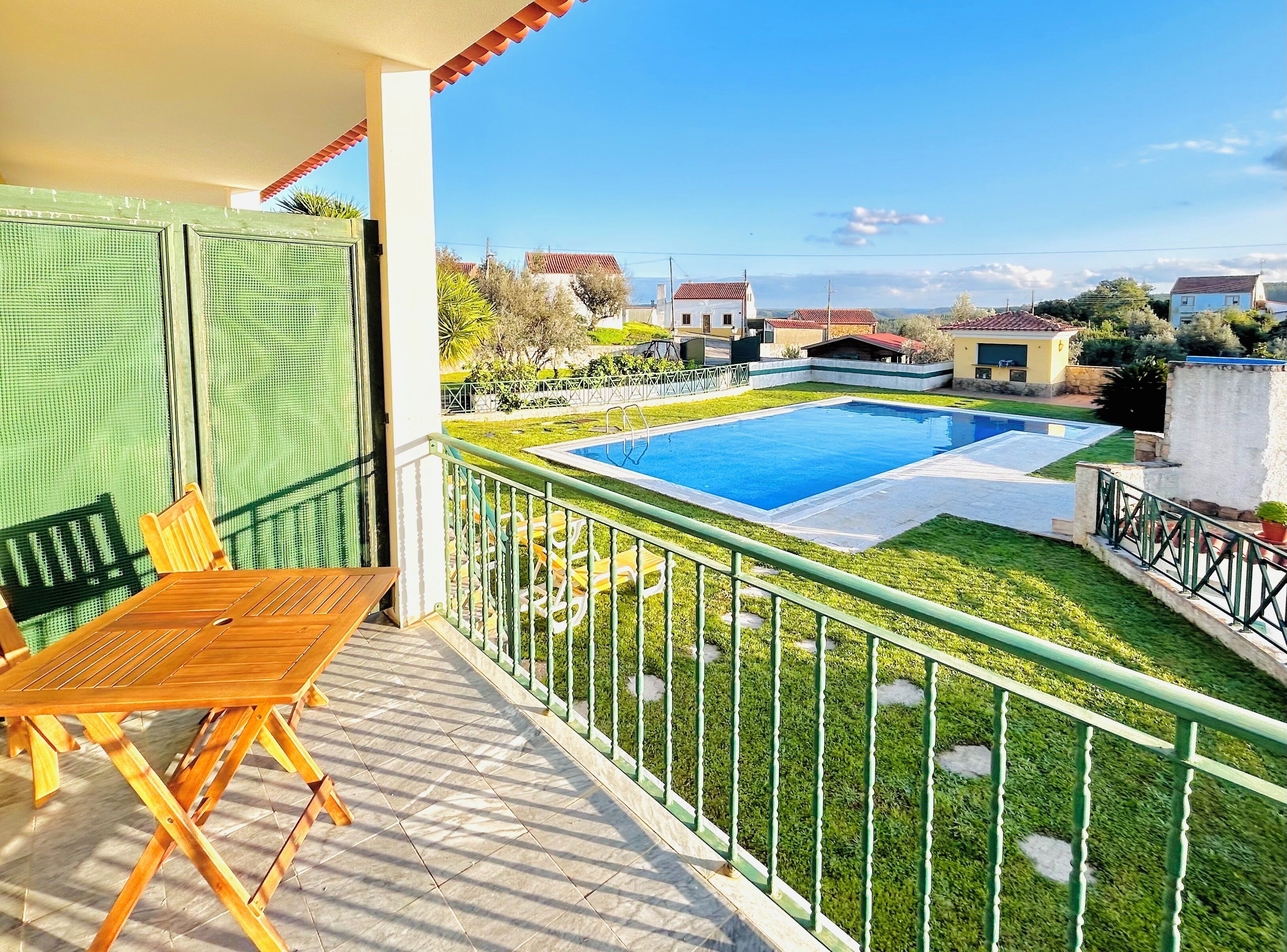 Un balcón con vista a una piscina, una mesa de madera y una silla.