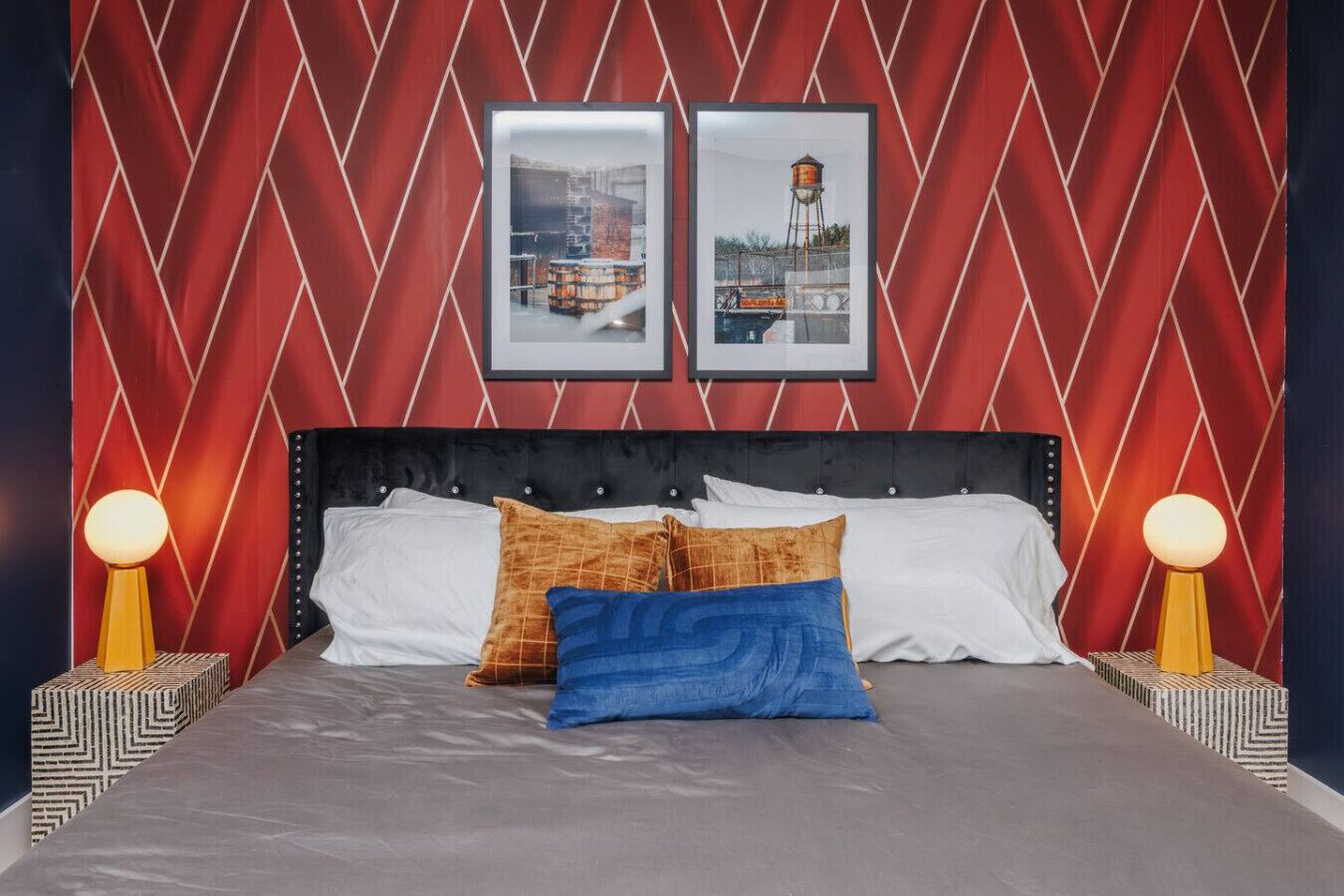 A bed with a black headboard, white and blue pillows, and two bedside lamps.
