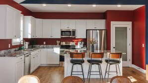 A modern kitchen with white cabinets, a central island, and a dining area with a black table and brown placemats.