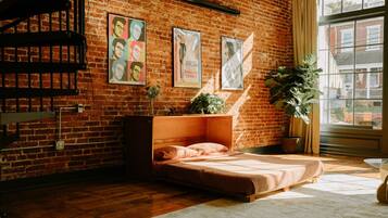 Une pièce chaleureuse avec un mur en briques, un lit avec une tête de lit, une fenêtre avec des rideaux et une plante.