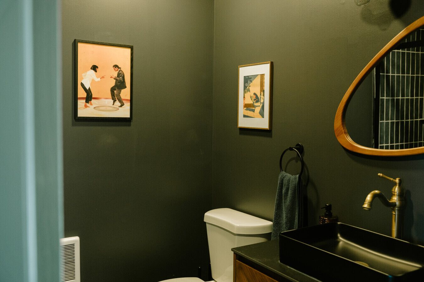 A bathroom with a toilet, sink, and framed artwork on the wall.