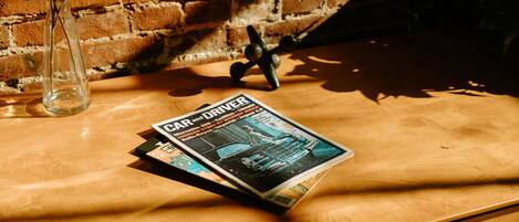 Una revista titulada "CAR and DRIVER" sobre una mesa de madera, con un muro de ladrillo al fondo.