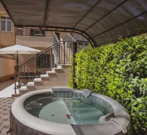 A hot tub with a glass enclosure, a staircase, and a covered outdoor area with a hedge.