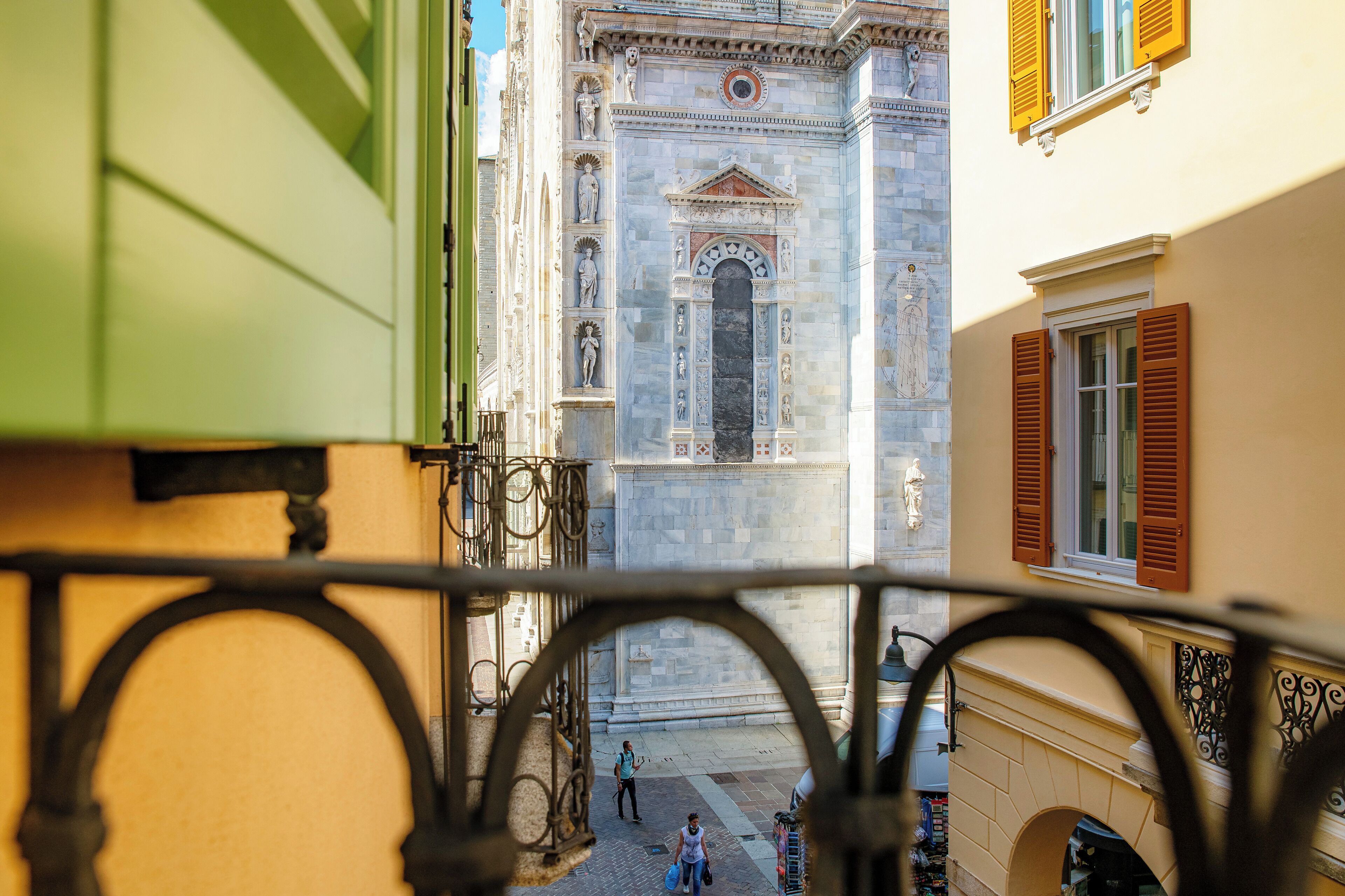 A view through a metal gate of a historic building with classical architecture, including statues and detailed stonework.