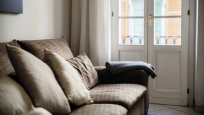 A beige sofa with multiple cushions, a blanket, and a white door with a metal handle. - Centro Storico (Como)