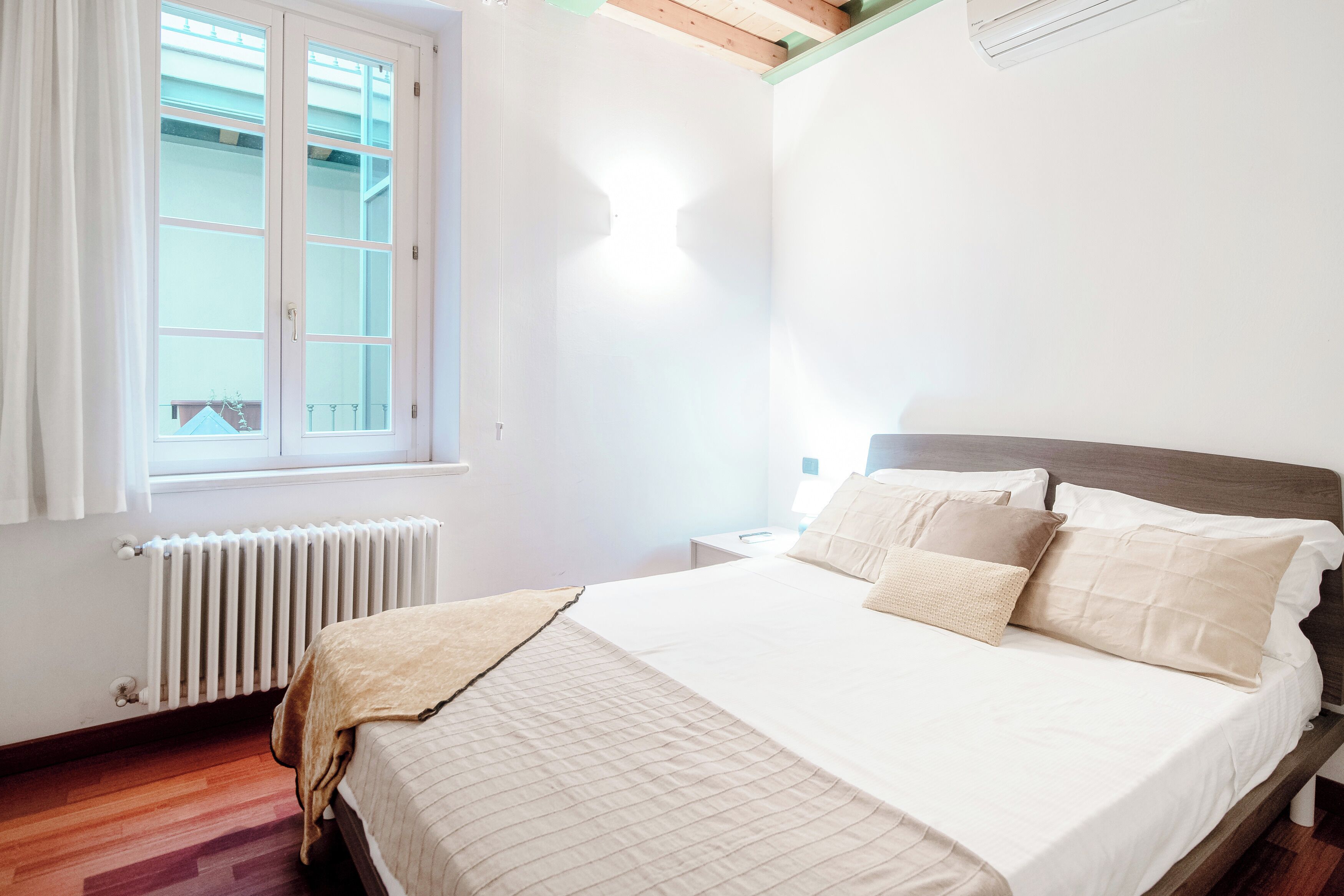 A bedroom with a bed, a window, a radiator, and a wooden floor.