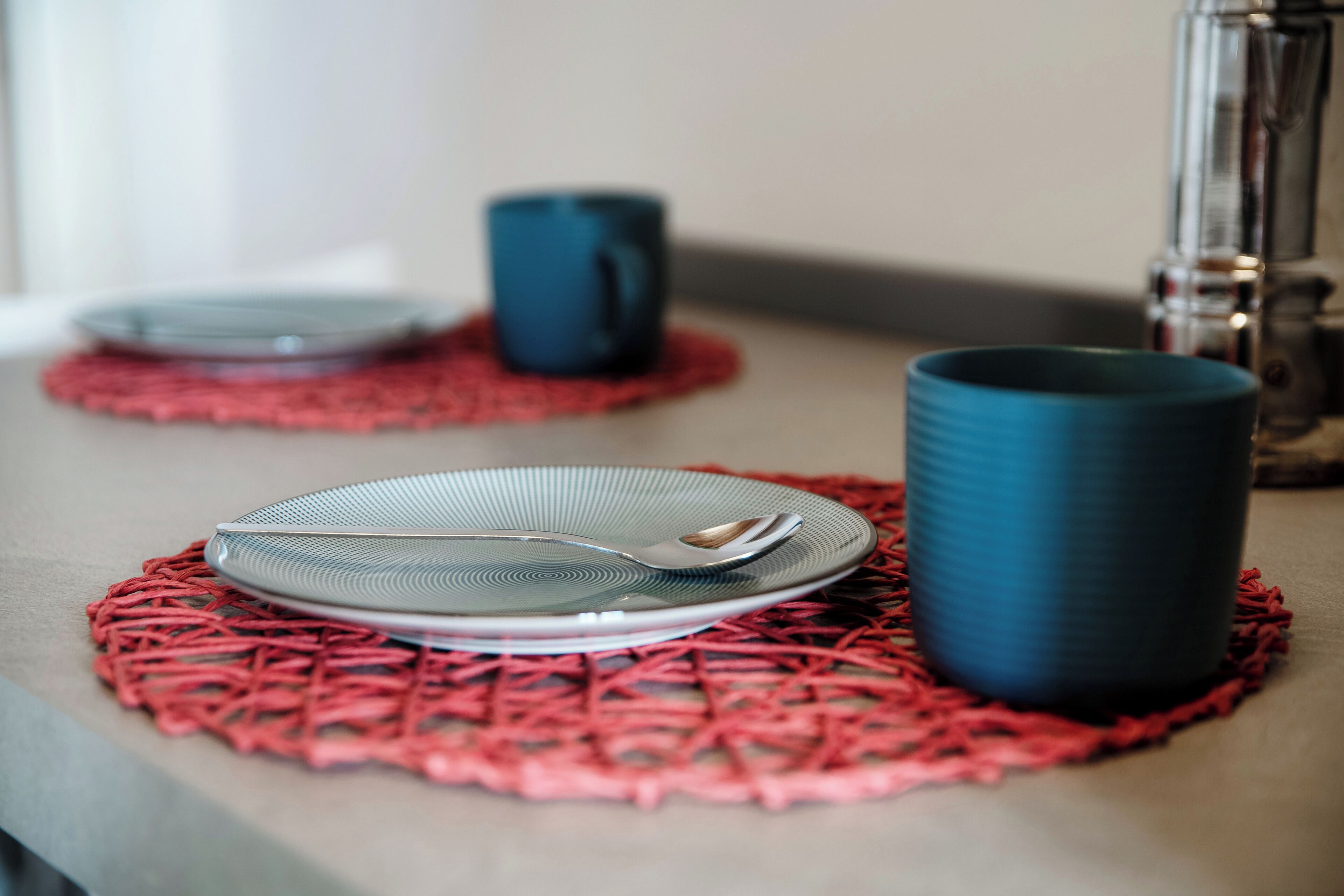 Ein Esstisch mit Teller, Schüssel und Tasse auf einer roten Tischmatte.