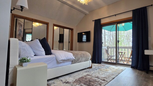 Ein Schlafzimmer mit Bett, Schreibtisch, Stuhl, Fernseher und einem Balkon mit Blick.