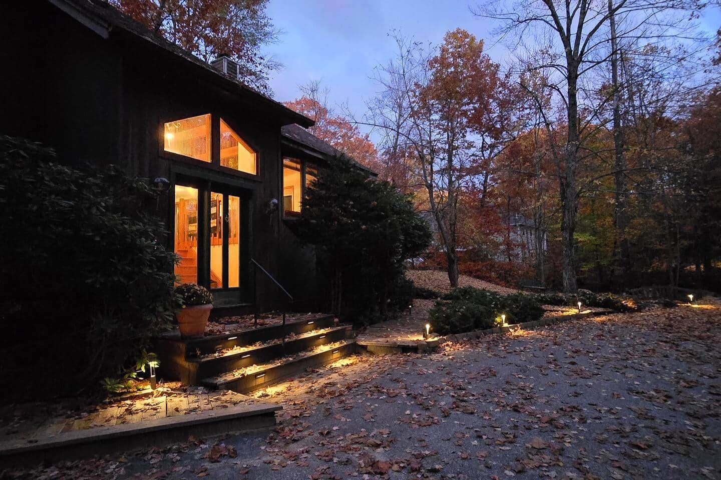 A house with a dark exterior, large windows, and a well-lit entrance.