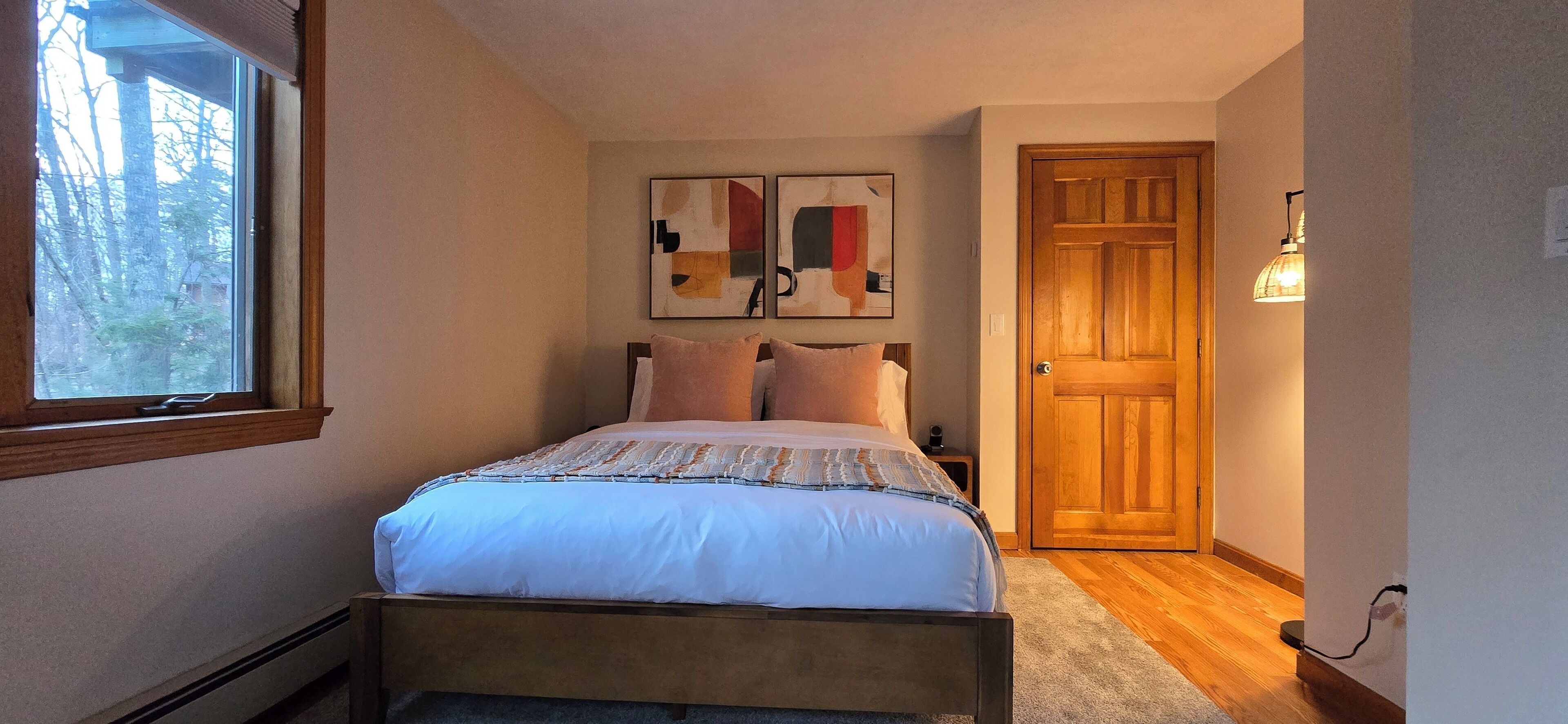 Un dormitorio con una cama, un ventanal, una puerta y dos obras de arte colgadas en la pared.