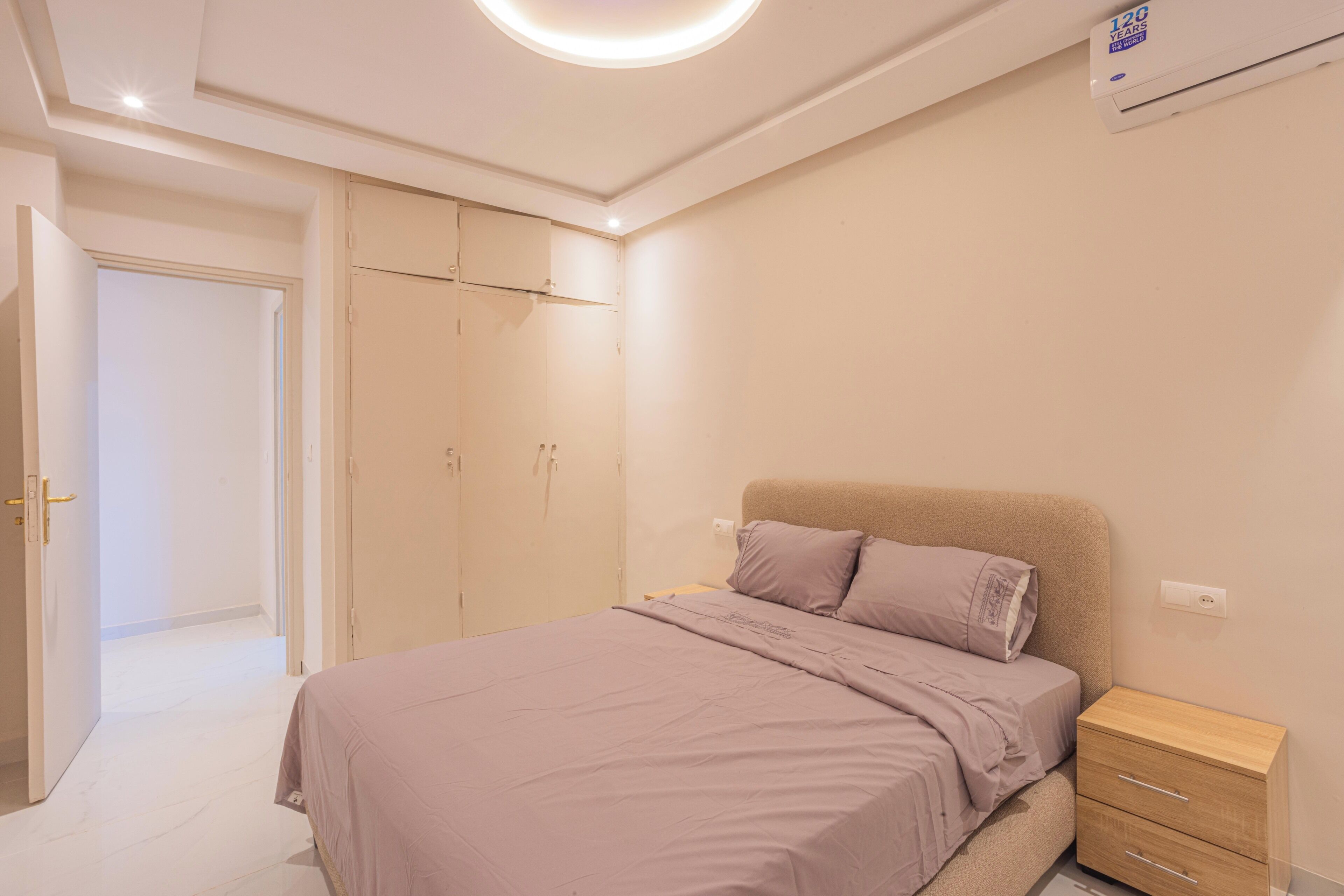 A bedroom with a bed, a nightstand, a wardrobe, and an air conditioning unit.
