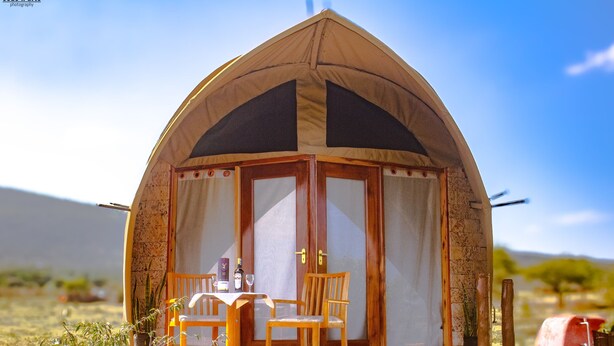 Tienda en forma de cúpula con una mesa y sillas afuera, ubicada en un área verde bajo un cielo despejado.