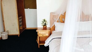 Un dormitorio con una cama de madera, una mesita de noche con un jarrón, un armario y una lámpara fijada a la pared.