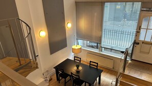 Ein Essbereich mit Tisch, Stühlen, einer Lampe, einem Heizkörper und einem Fenster mit Jalousien.