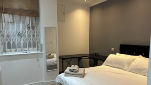 Ein Schlafzimmer mit Bett, Nachttisch, Spiegel und einem Fenster mit Jalousien.