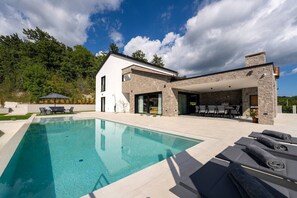 Une maison moderne dotée d’une piscine, d’un espace salon extérieur et d’une façade en pierre.