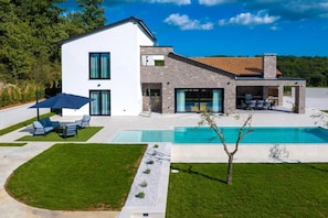 Une maison moderne à deux étages, dotée d’une piscine, d’un espace salon extérieur et d’une pelouse bien entretenue.