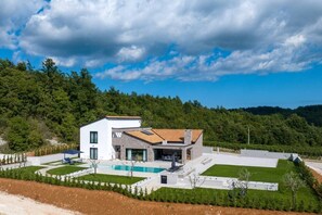 A modern two-story house with a swimming pool, surrounded by a landscaped garden and forested hills. - Villa Angelina – luxury villa offering pool with shallow section and Media Room (Mandalencici)