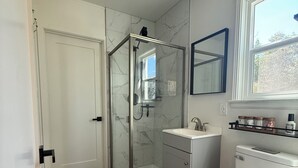 Une salle de bain avec une douche à parois de verre, des toilettes blanches, un lavabo et un miroir au-dessus du lavabo.