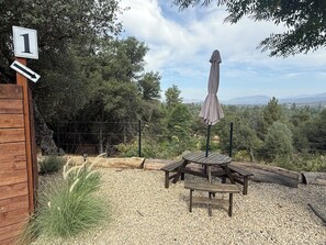 A wooden deck with a picnic table and umbrella, surrounded by gravel and greenery.
