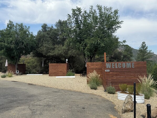 A wooden welcome sign with a directional arrow, surrounded by gravel and desert plants.